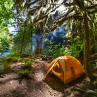 A woman cooks near the fire while two children play in the tent at a backcountry campsite near a stream. Siouxon Creek, Gifford Pinchot National Forest, Washington State.
