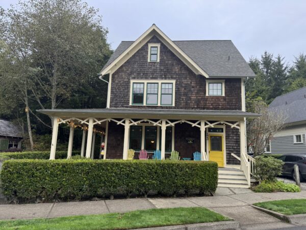 Exterior of the “Once Upon a Time” vacation rental home in Seabrook, Washington, a large gray-and-white coastal-style house with a front porch and tall windows surrounded by trees.