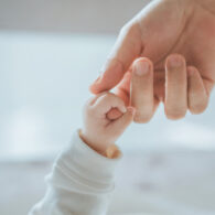Close-up little hand of child baby holding hand of mother, A newborn holds on to mom's, dad's finger, Love and relationship with infant, Care and support, Dreaming and protection