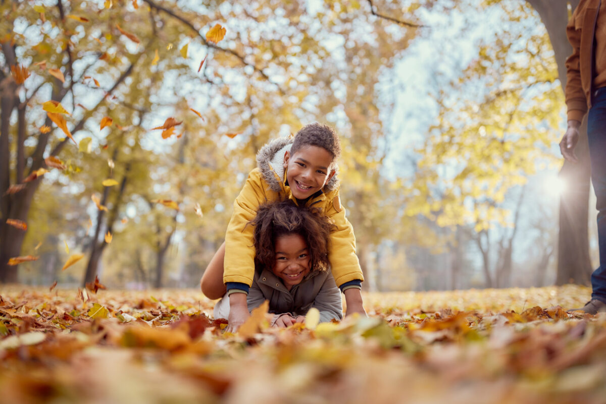 Happy kids having fun while playing in autumn leaves at the park and looking at camera.