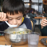 Kid sits at a table eating a bowl of pho