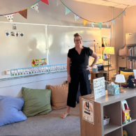 Woman stands in front of white board in children's classroom.